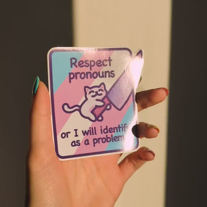 A close-up of the sticker. It reads 'Respect pronouns or I will identify as a problem'. It has a drawing of a cute white cat holding a knife.