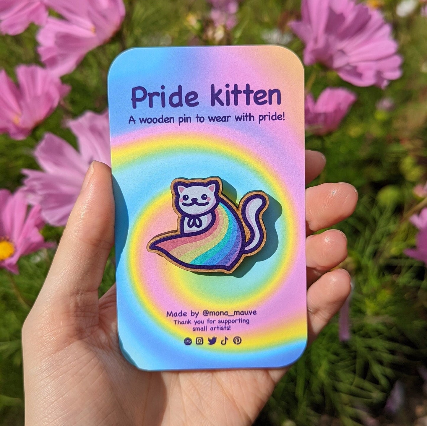 A cute wooden badge with an illustration of a cat wearing a rainbow pride cape. The backing card reads: "Pride kitten! A wooden pin to wear with pride"