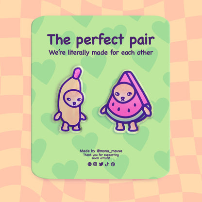 A set of two acrylic pins. One pin is a cat wearing a banana costume, the other - a cat wearing a watermelon costume. The backing card reads: "The perfect pair. We're literally made for each other"